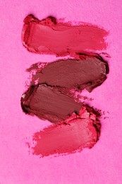 Smears of bright lipsticks on pink background, top view