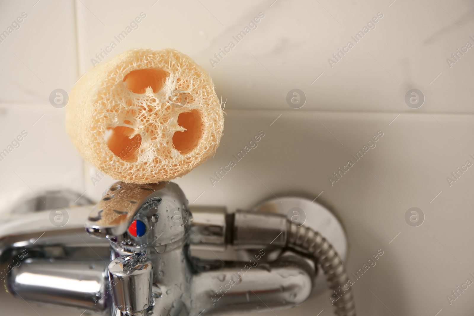 Photo of Natural loofah sponge on faucet in bathroom, closeup