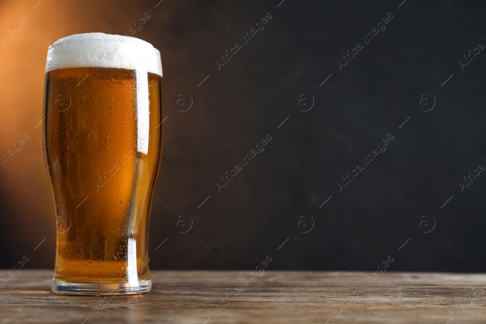 Photo of Cold tasty beer on wooden table against dark background. Space for text