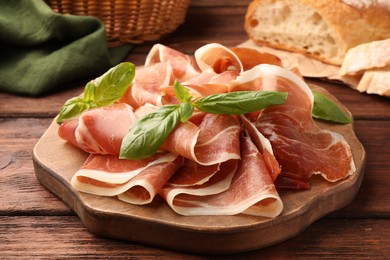 Photo of Slices of tasty cured ham and basil on wooden table, closeup