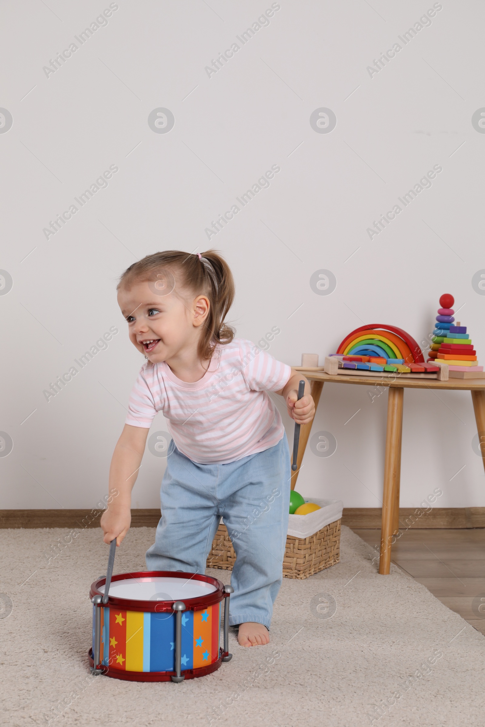 Photo of Cute little girl playing with drum and drumsticks at home