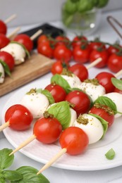 Photo of Caprese skewers with tomatoes, mozzarella balls, basil and pesto sauce on table, closeup. Space for text