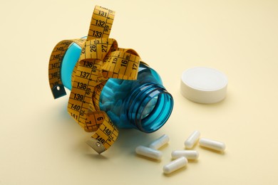 Photo of Jar of weight loss pills and measuring tape on beige background