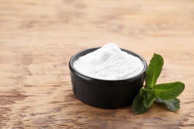 Photo of Sweet fructose powder and mint leaves on wooden table