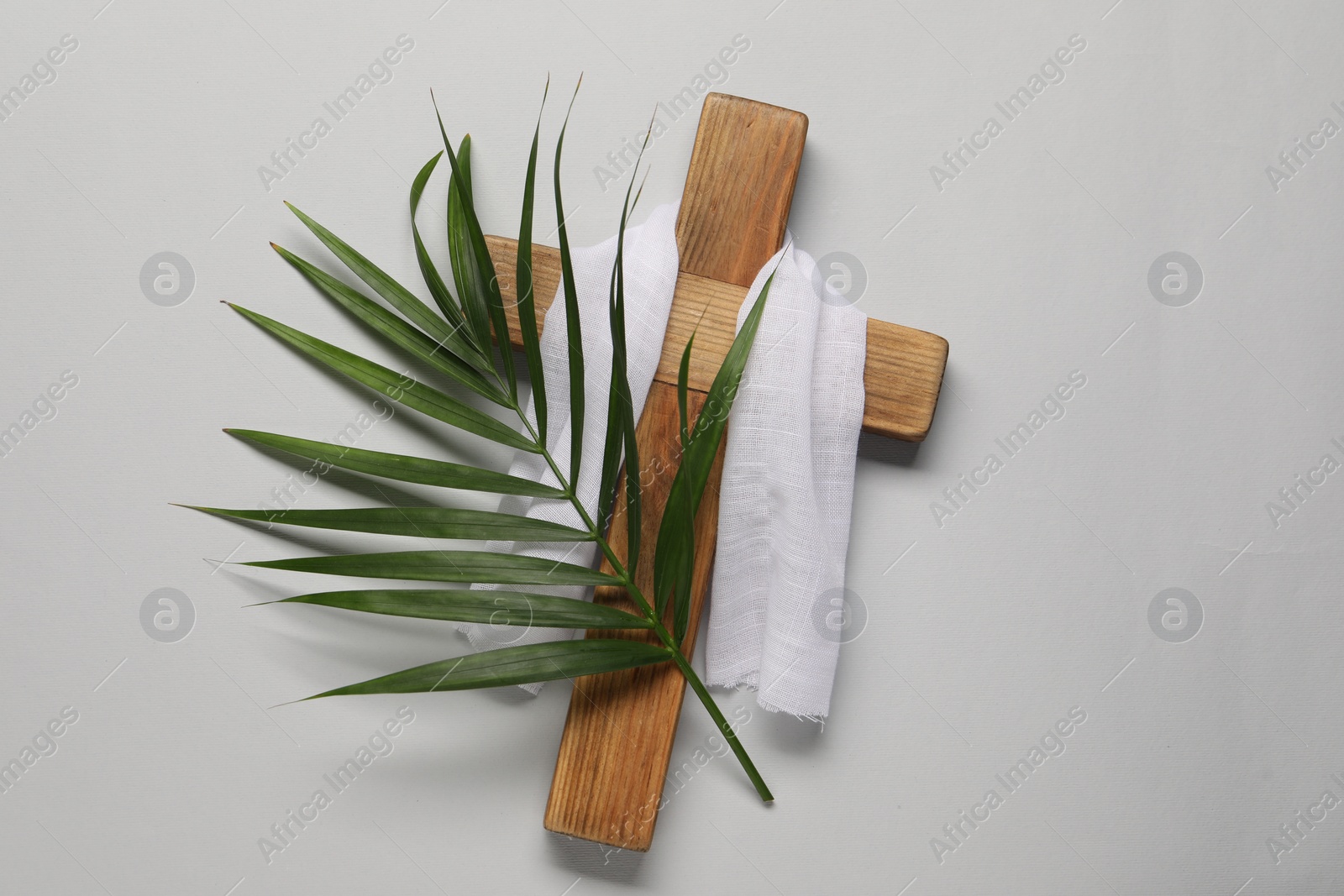 Photo of Wooden cross, white cloth and palm leaf on light grey background, top view. Easter attributes
