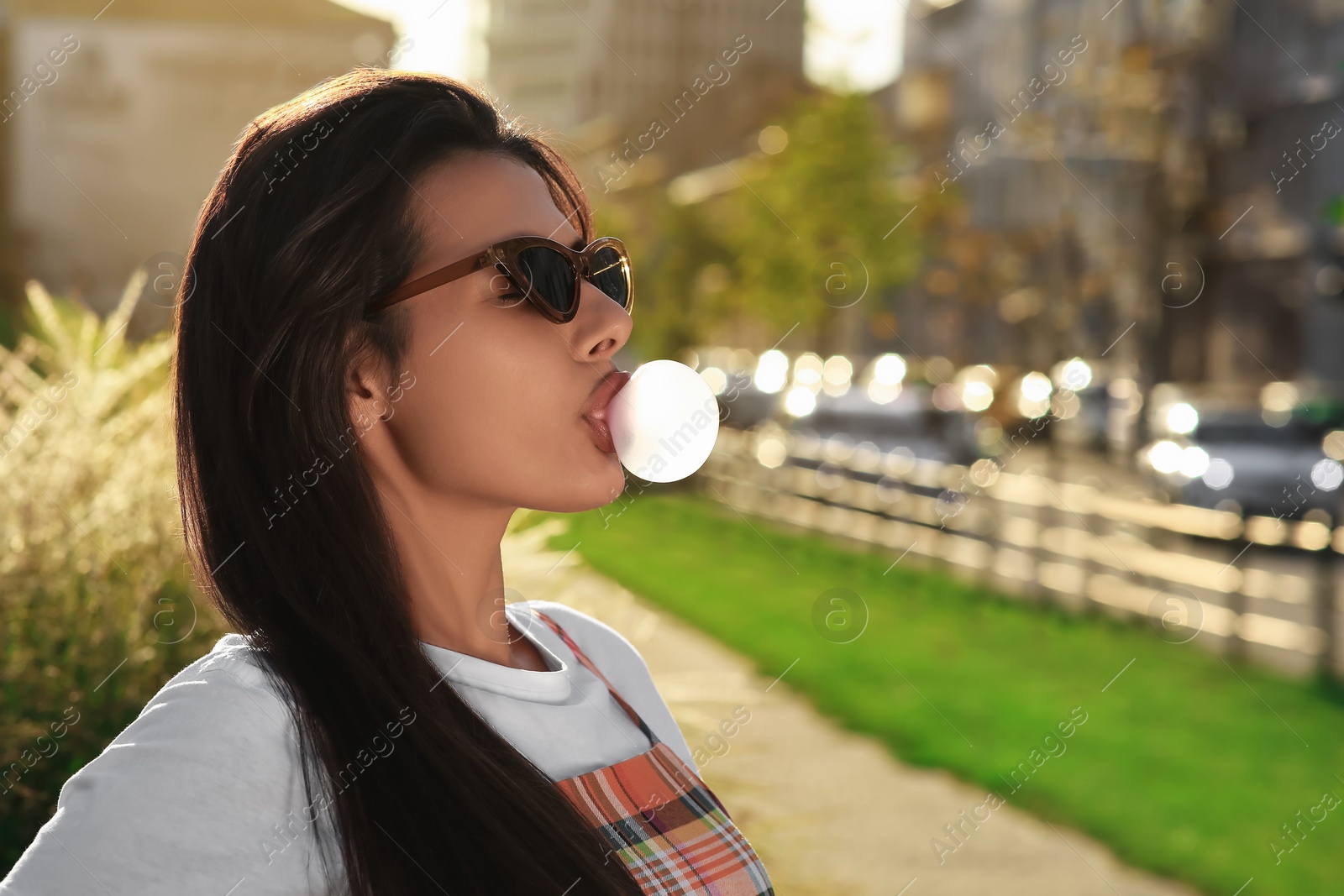 Photo of Beautiful woman blowing gum on city street, space for text