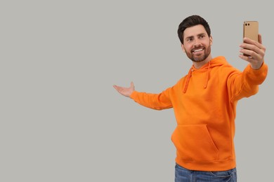 Photo of Smiling man taking selfie with smartphone on grey background, space for text