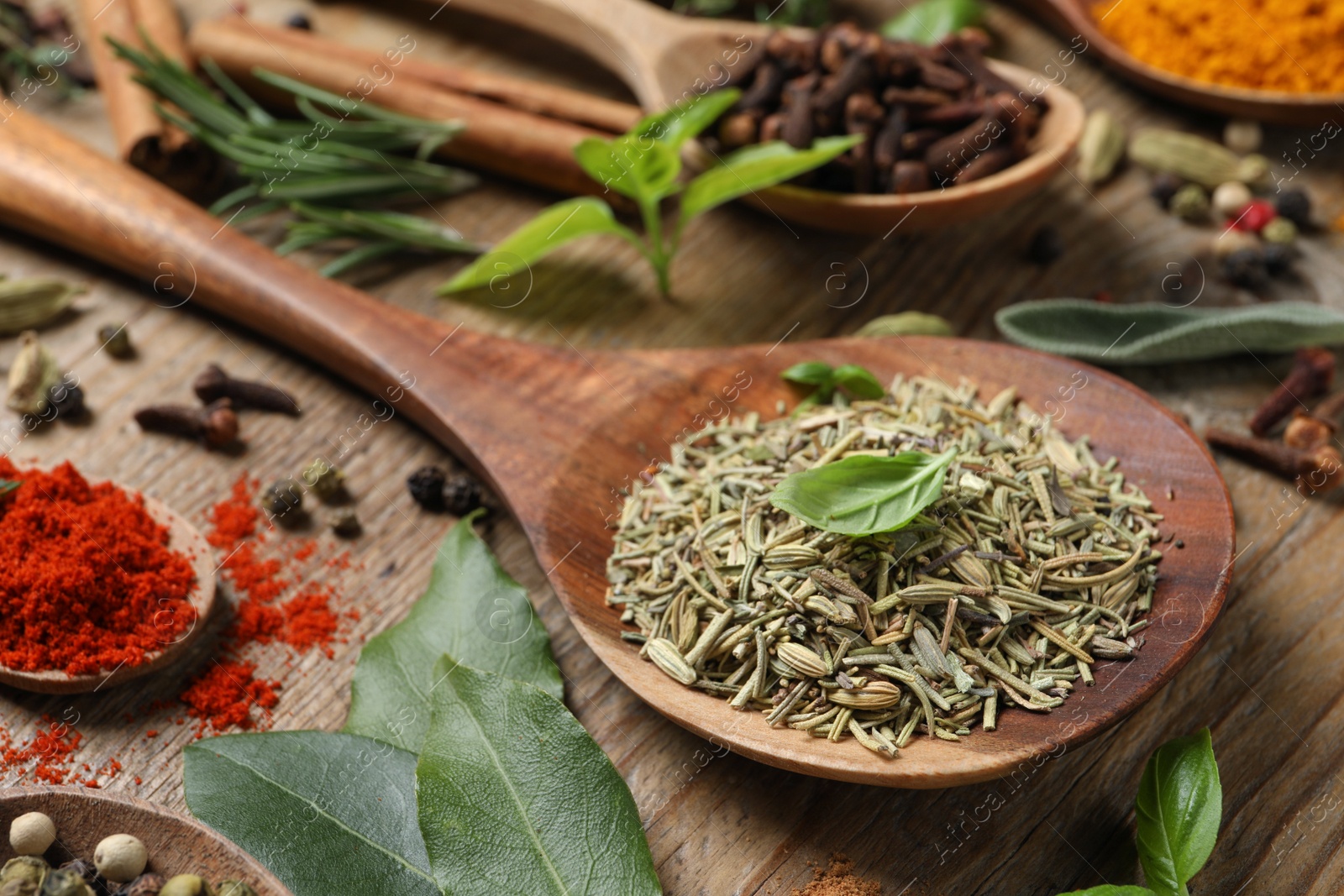 Photo of Different herbs and spices with spoons on wooden table, closeup