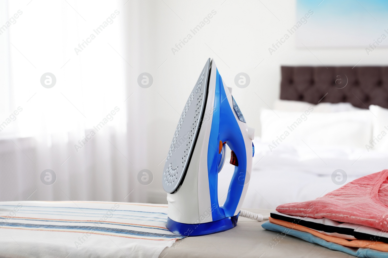 Photo of Modern electric iron on board indoors, space for text. Household appliance