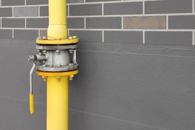 Photo of Yellow gas pipe with valve near brown wall outdoors, space for text