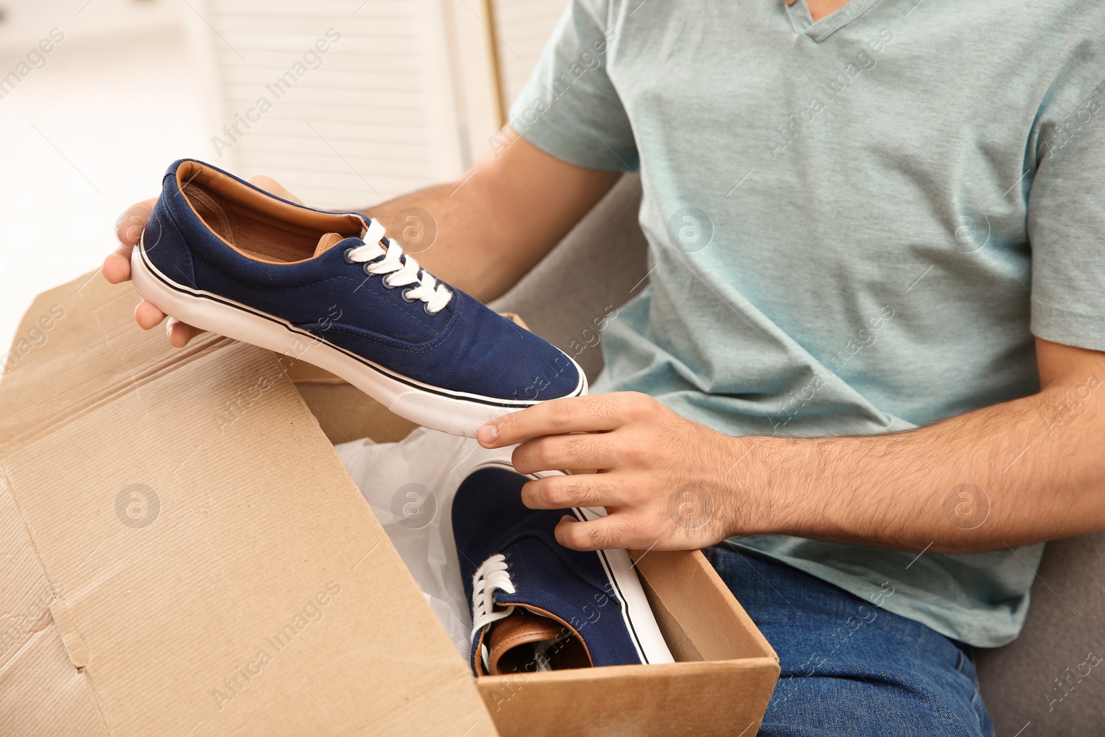 Photo of Young man opening parcel with shoes at home, closeup