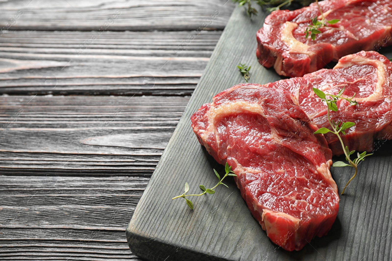Photo of Fresh raw meat steaks on black wooden table. Space for text