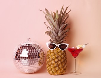Image of Funny pineapple with sunglasses, cocktail and disco ball on pink background. Summer party