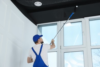 Photo of Worker in uniform painting ceiling with roller indoors