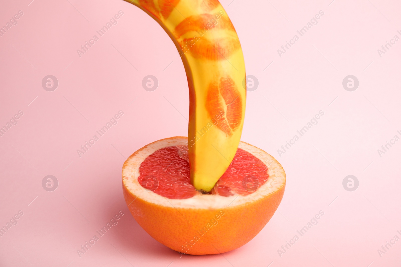 Photo of Fresh banana with red lipstick marks and grapefruit on pink background. Sex concept