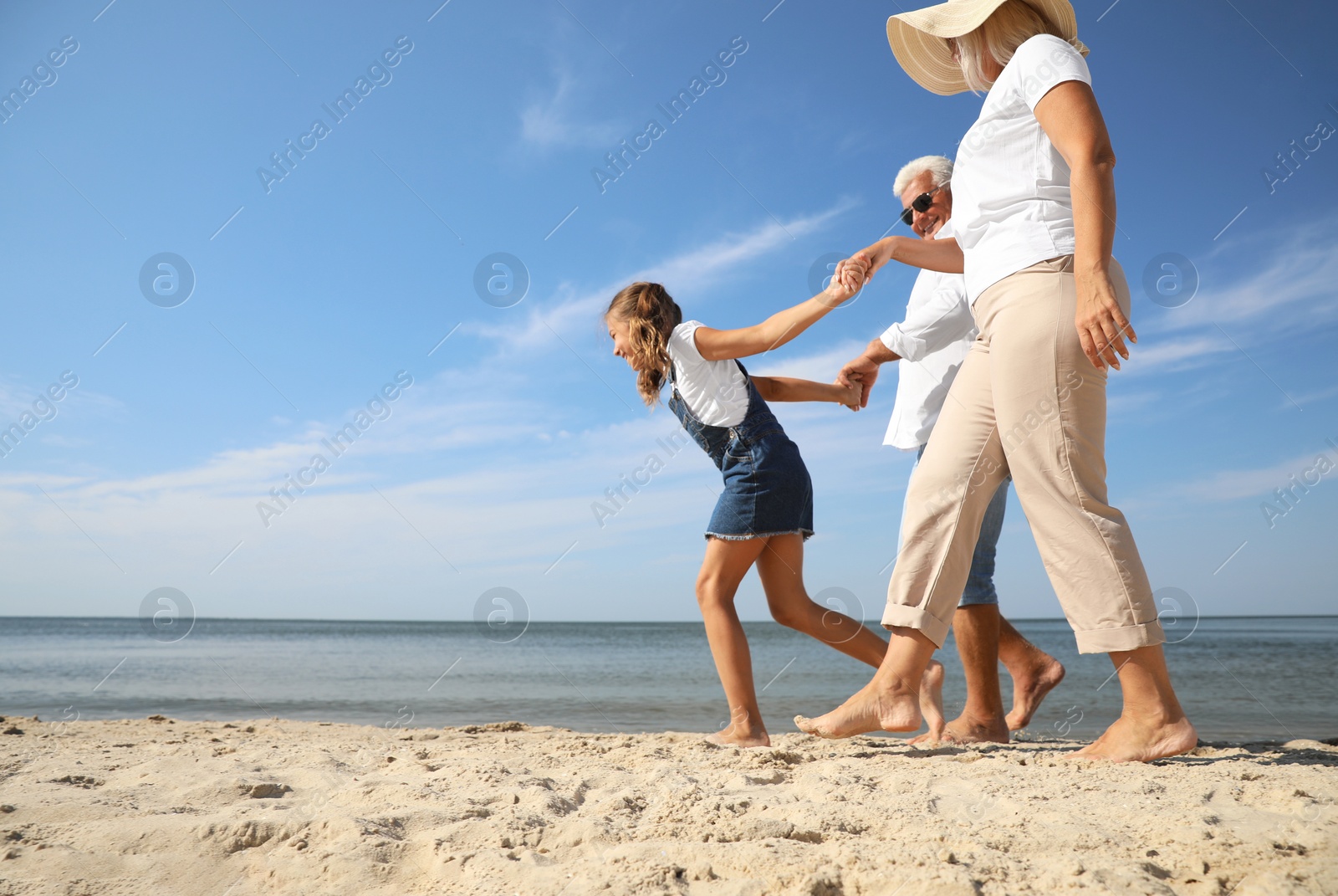 Photo of Cute little girl with grandparents spending time together on sea beach