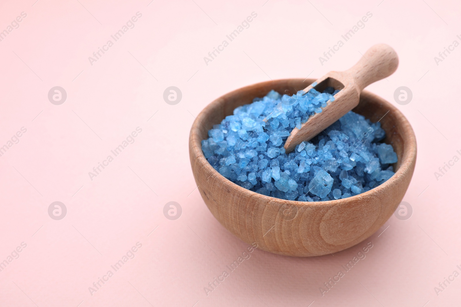 Photo of Bowl and scoop with blue sea salt on pale pink background. Space for text