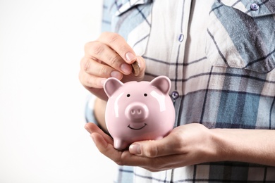 Photo of Woman putting coin into piggy bank on light background, closeup. Money savings