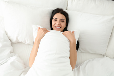 Photo of Young woman with pillow in bed, top view. Lazy morning