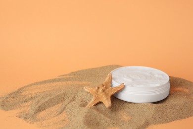 Photo of Jar with cream and starfish on sand against orange background, space for text. Cosmetic product