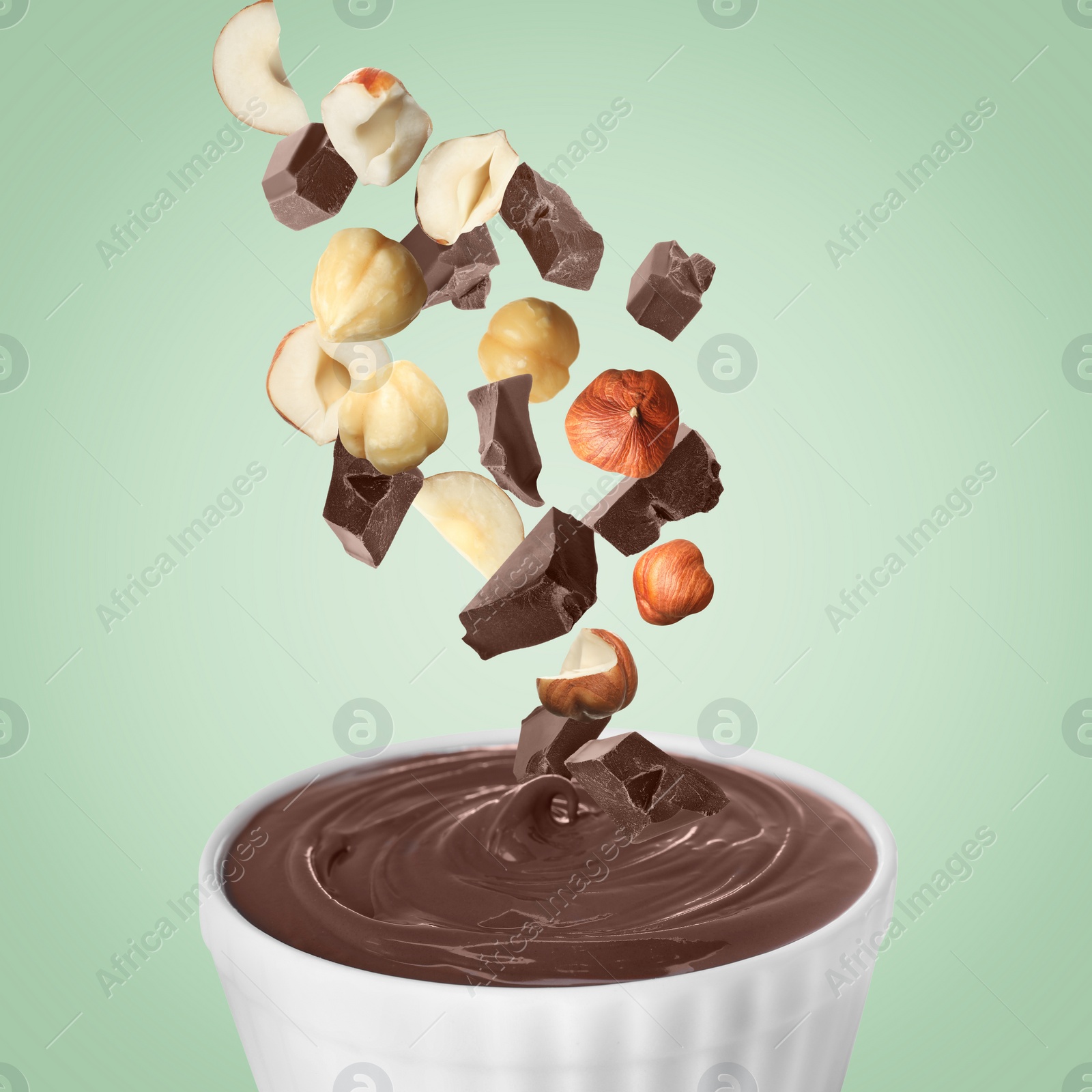 Image of Making yummy chocolate paste. Hazelnuts and pieces of chocolate falling into bowl on light green background