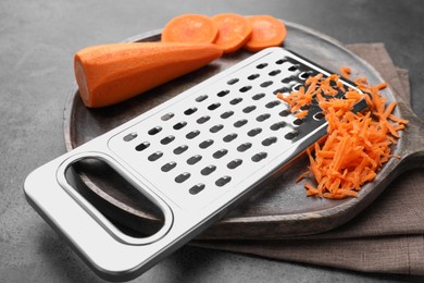 Grater and fresh ripe carrot on grey table, closeup