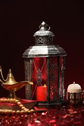 Arabic lantern, Quran, misbaha, burning candle and Aladdin magic lamp on shiny red table