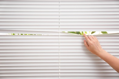 Photo of Woman separating slats of window blinds, closeup