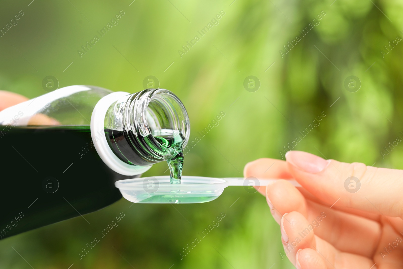 Photo of Woman pouring syrup from bottle into dosing spoon on blurred background, closeup. Cold medicine