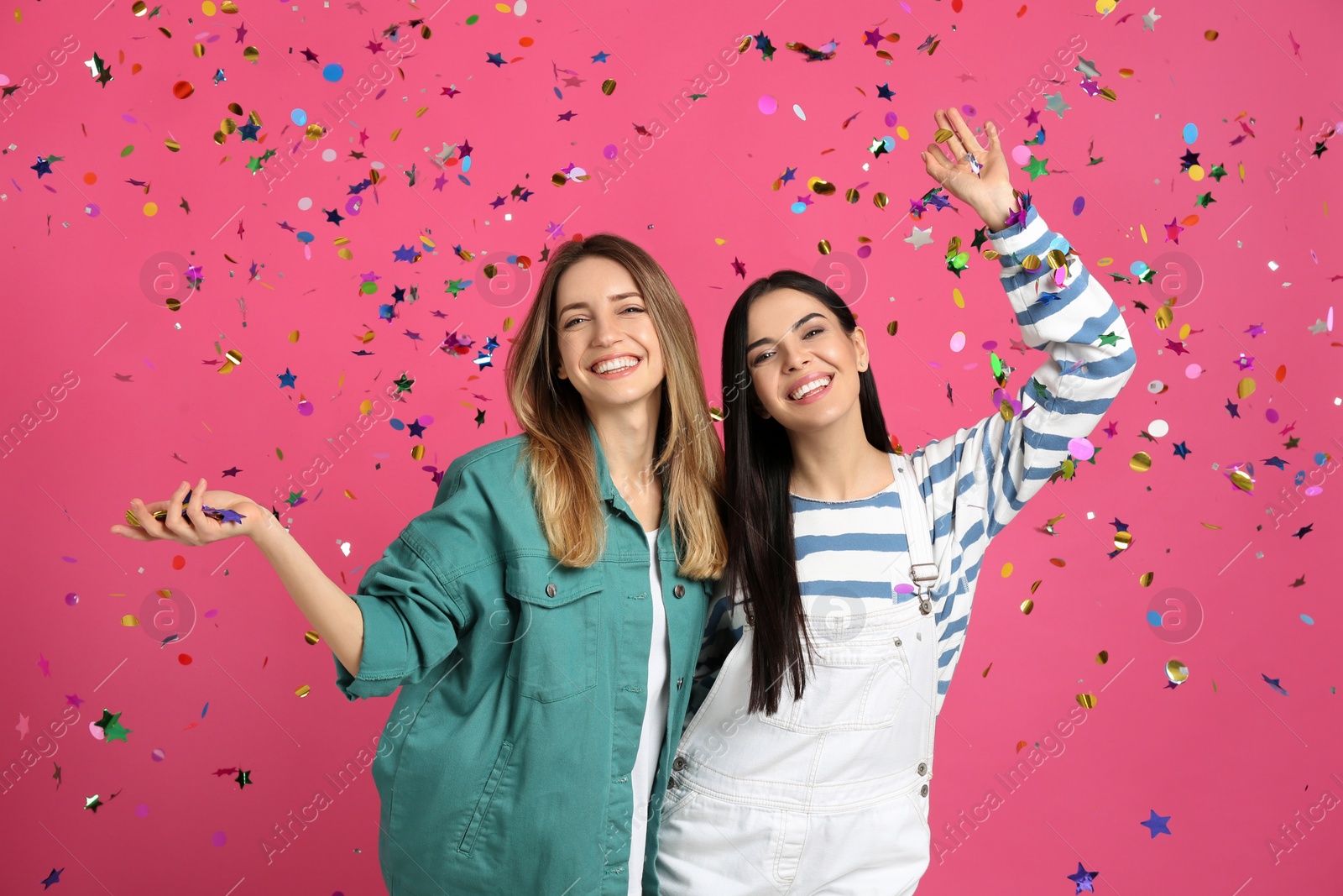 Photo of Happy women and falling confetti on pink background