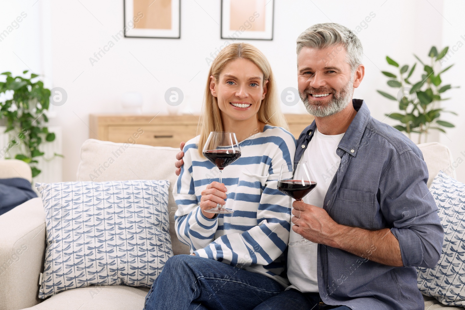 Photo of Happy affectionate couple with glasses of wine on sofa at home, space for text. Romantic date