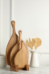 Photo of Wooden cutting boards, kitchen utensils and dishware on white marble table