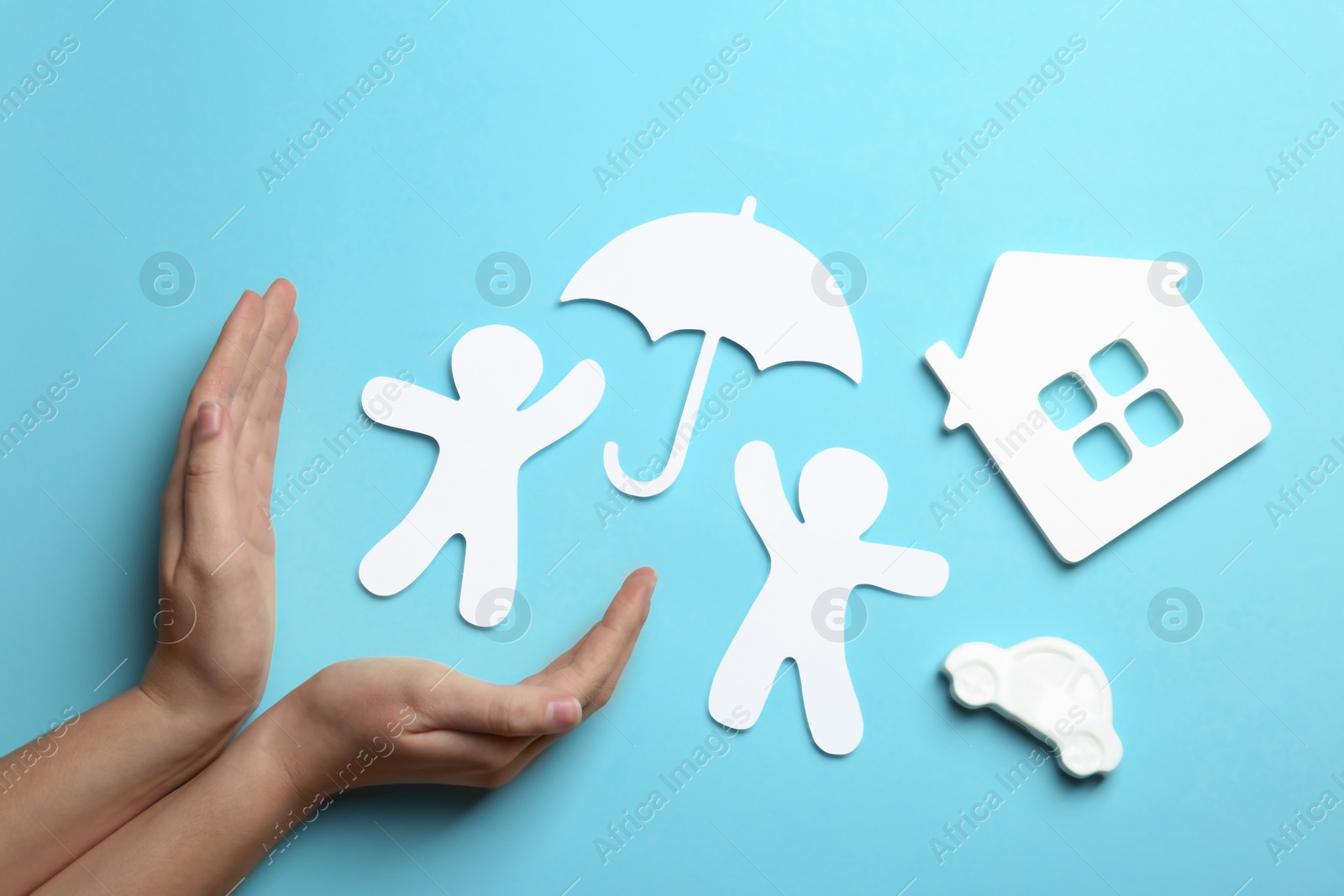 Photo of Woman holding hands near paper silhouettes of people with umbrella, car and house on color background, top view. Life insurance concept