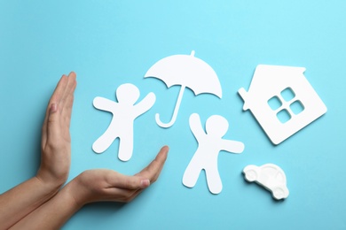 Woman holding hands near paper silhouettes of people with umbrella, car and house on color background, top view. Life insurance concept