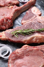Photo of Fresh raw beef cuts with rosemary and onion on table, closeup
