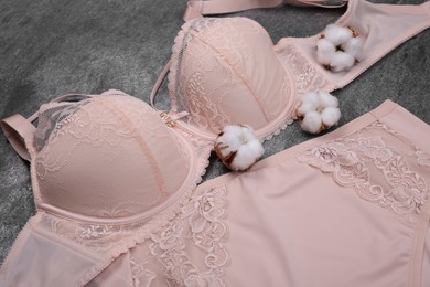 Photo of Elegant beige plus size women's underwear and cotton flowers on grey background, closeup