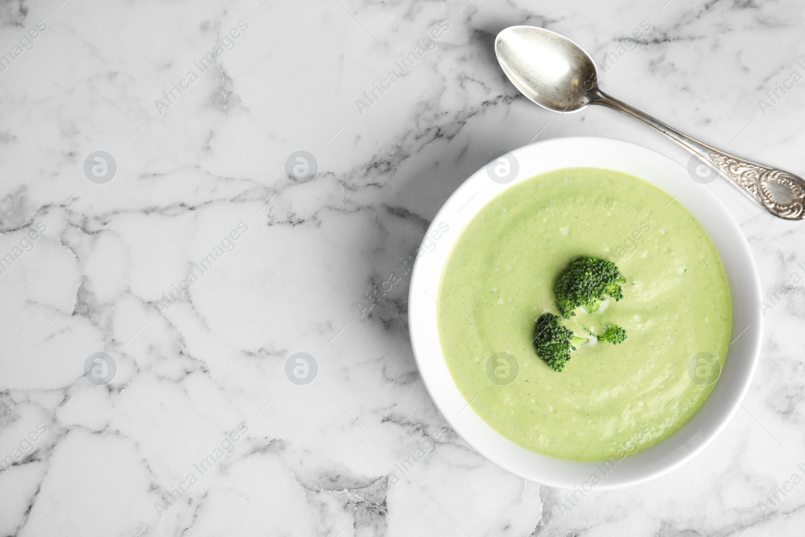 Photo of Delicious broccoli cream soup served on white marble table, flat lay. Space for text