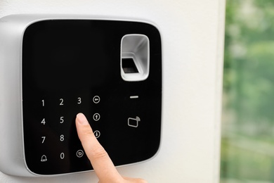 Photo of Young woman entering code on alarm system keypad indoors