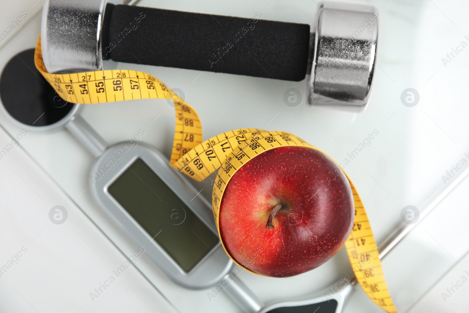 Scales, apple, measuring tape and dumbbell on white table, top view Photo of Scales, apple, measuring tape and dumbbell on white table, top view