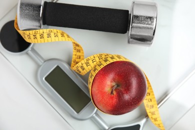 Photo of Scales, apple, measuring tape and dumbbell on white table, top view