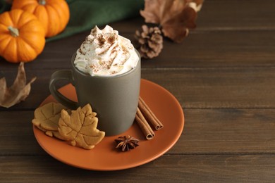 Photo of Tasty pumpkin spice latte with whipped cream in cup and cookies on wooden table. Space for text