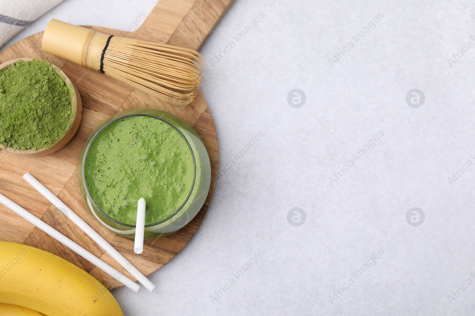 Photo of Glass of tasty matcha smoothie, powder, bamboo whisk and straws on light table, flat lay. Space for text