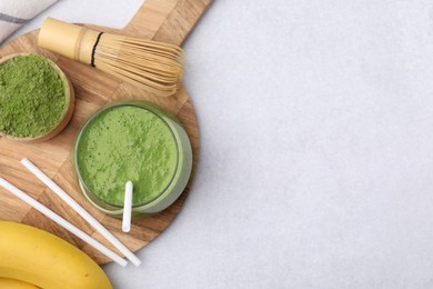 Glass of tasty matcha smoothie, powder, bamboo whisk and straws on light table, flat lay. Space for text