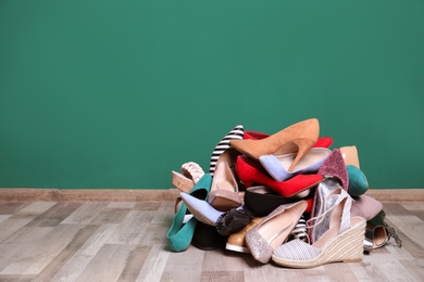 Photo of Heap of different shoes on floor against color wall. Space for text