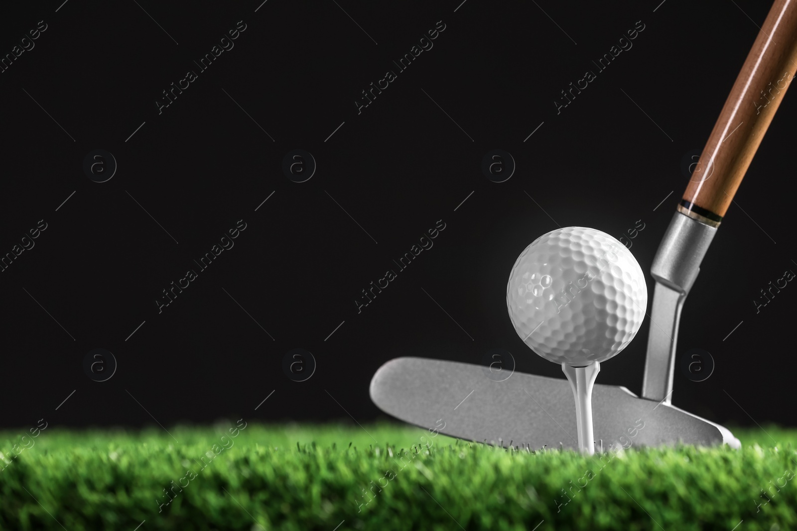 Photo of Hitting golf ball with club on artificial grass against black background, space for text