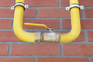 Photo of Yellow gas pipe on red brick wall outdoors, closeup