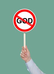 Image of Atheism concept. Man holding prohibition sign with crossed out word God on pale green background