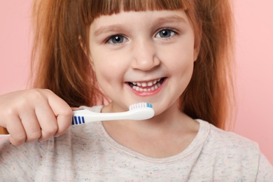 Little girl brushing teeth on color background, closeup