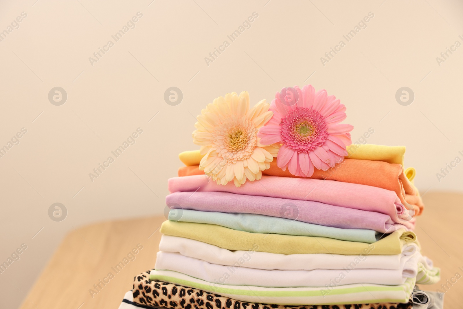 Photo of Stack of clean clothes and flowers on table. Space for text