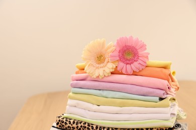 Stack of clean clothes and flowers on table. Space for text